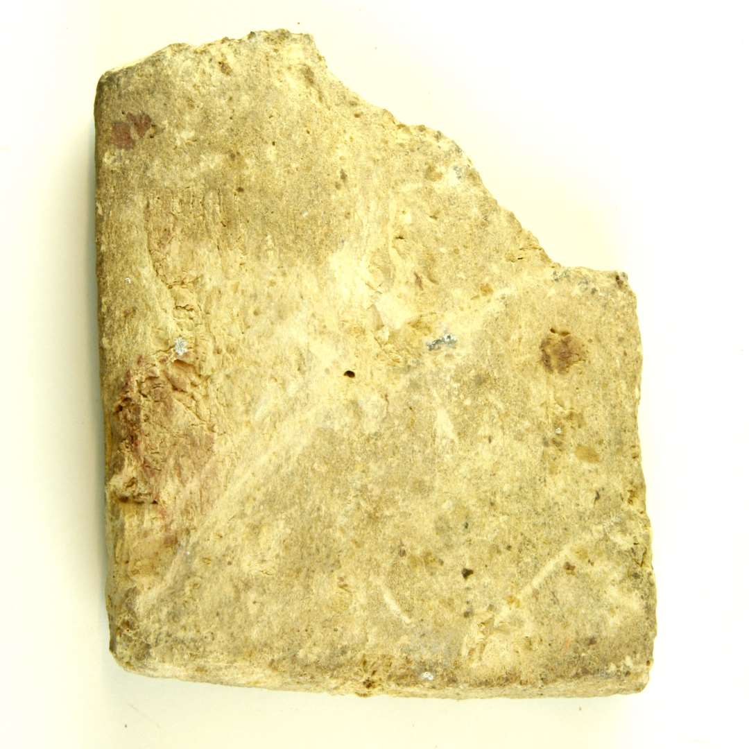 Fragment af gulbrændt mursten, stærkt nedslidt. Bev. længde: 12,5 cm. Bredde: 10 cm. Tykkelse 3,0 cm.