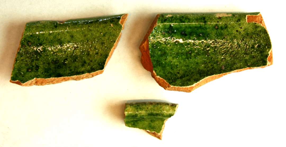 3 randskår fra fad eller skål af rødbrændt lergods med indersiden dækket af pibelersbegitning hvorover grønligspættet blyglasur. Sammenhørende med D14168.