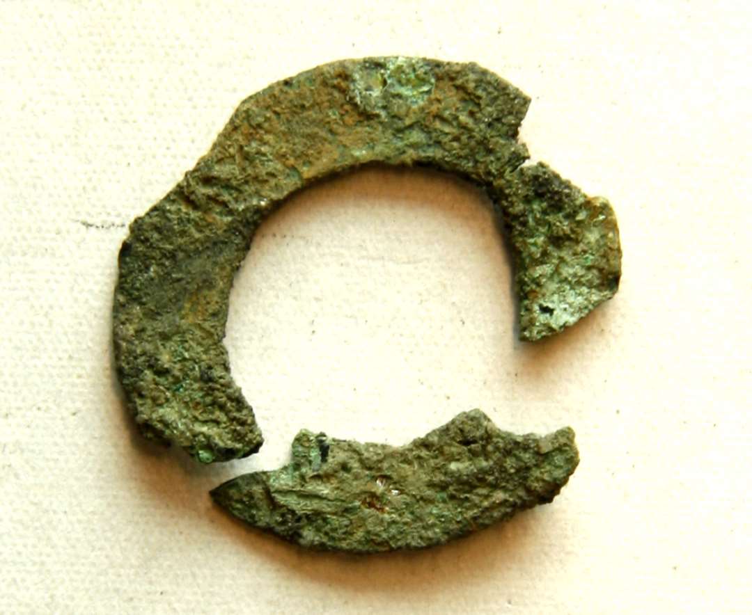 To samhørende fragmenter af tynd, flad cirkulær bronzering. Selve ringpladens br.: 0,5 cm. Ringens ydre diameter ca: 2,3 - 2,4 cm. Muligvis fragment af ringspænde.