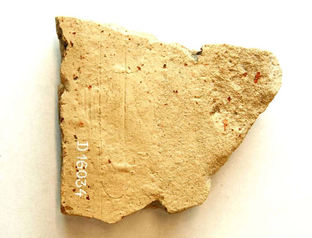 1 fragment af flad lerskive af grumsetgullig brændt lermasse hvori indgår knuste partikler og småstykker af rødbrændt ler. Kun den ene fladside og sammenstødende sidekant viser spor af ujævn afglatning, medens den modsatte side er ujævn og de øvrige kanter er brudflader.  Flisefragment ?. Største mål: 9 x 9,6 x 2,4 cm.