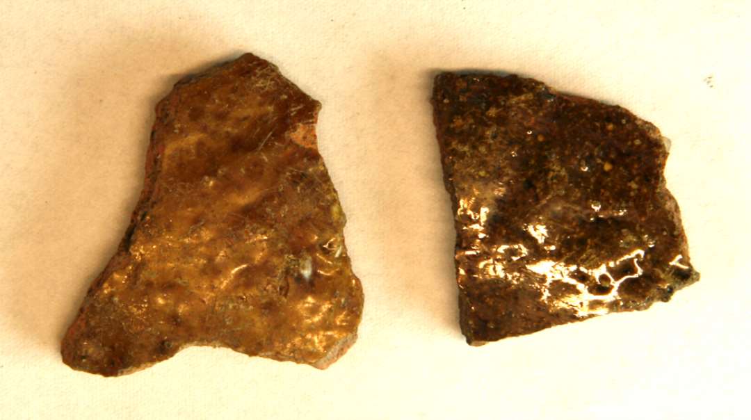 2 rødbrændte sideskår fra kander med klar, brunspættet blyglasur på yderside. Det ene er delvist reduceret i godset, og har 'hvide sten' i leret. 