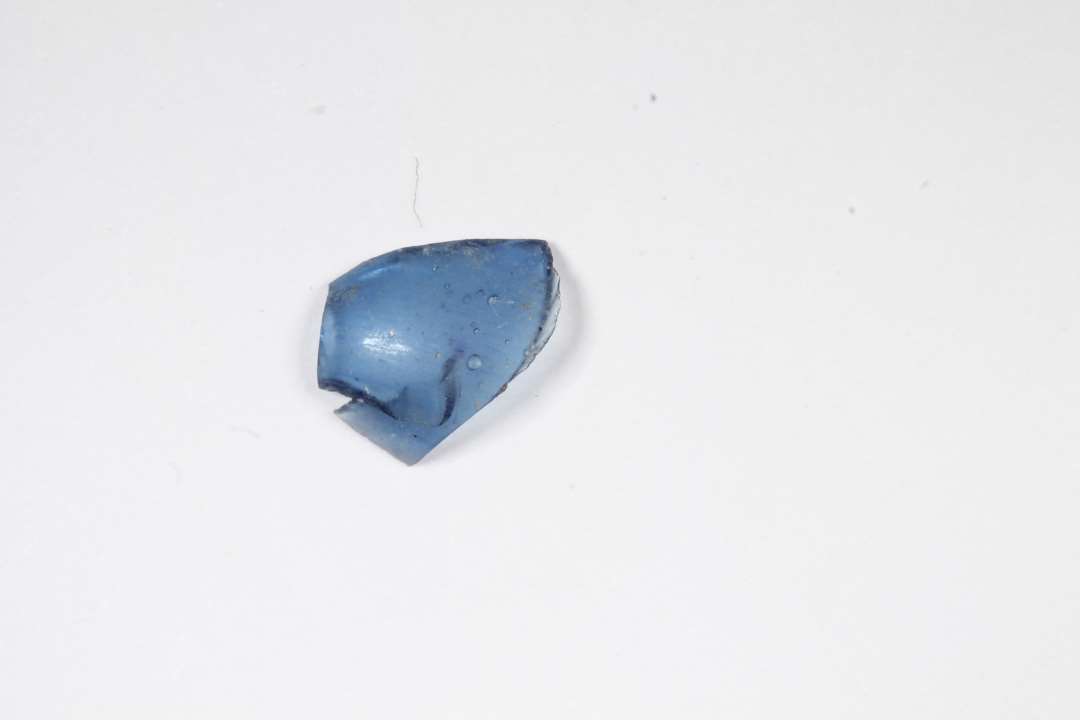 Fragnment af kugleformet, blæst, gennemsigtig blå glasperle. Største mål: 0,9 cm.