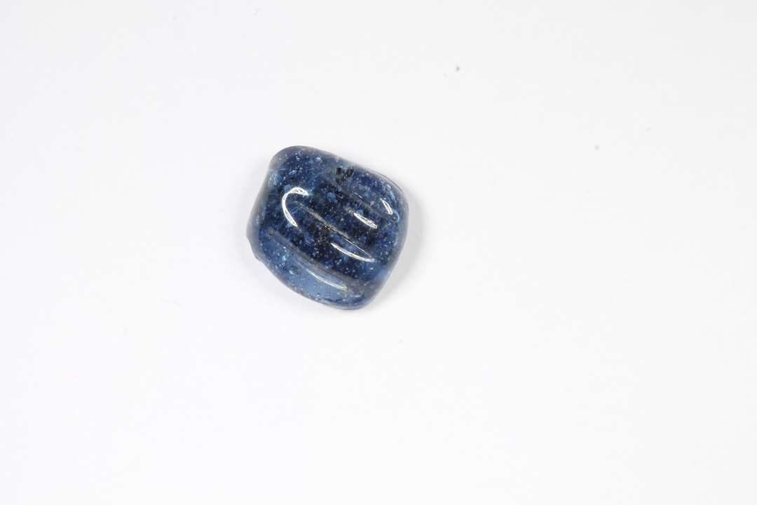 Fragment af ringformet, melonformet, gennemsigtig blå glasperle. Største mål: 0,6 cm.
