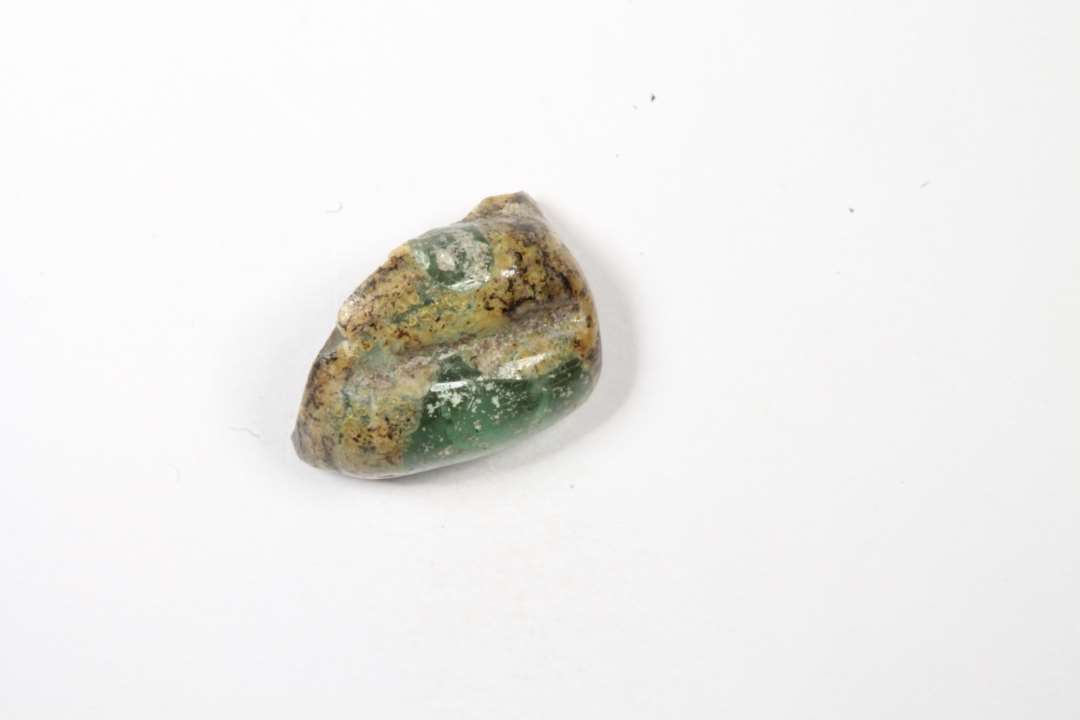 Fragment af cylindrisk melonformet, gennemsigtig grøn glasperle. Største mål: 1,1 cm.