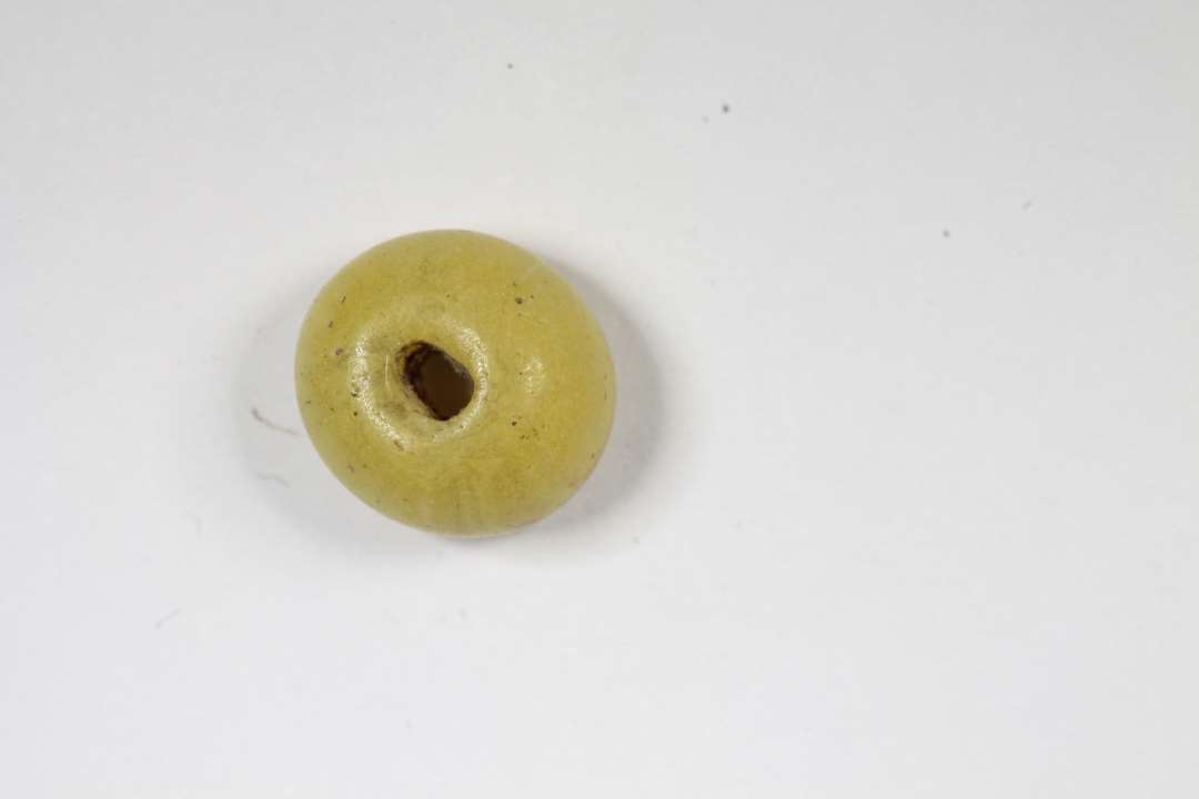 Ringformet, afskåret uigennemsigtig gul glasperle. Diameter: 0,8 cm.