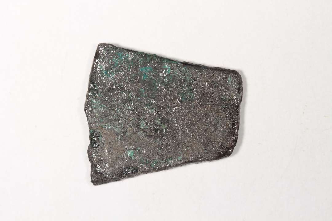 Et fladt stykke metal. Ligner bronze, men konserveringen mener sølv (en del sølvklorider på overfladen i forb. med kons). Største mål: 2,0x1,8x0,2 cm.