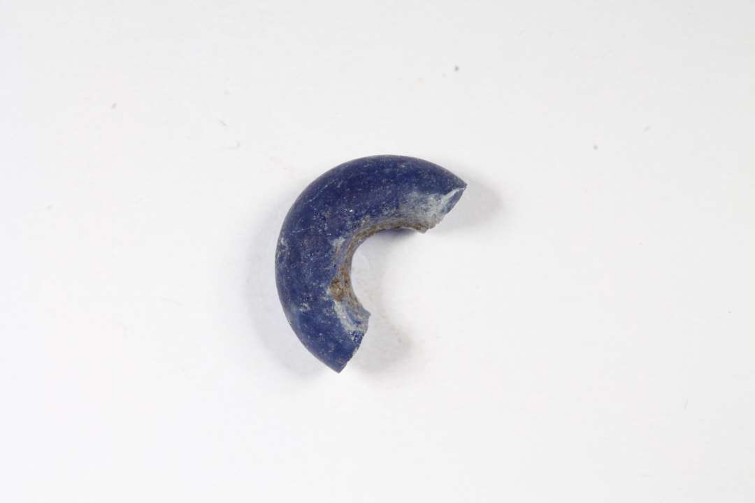 Halv ringformet, gennesigtig blå glasperle. Diameter: 1 cm.