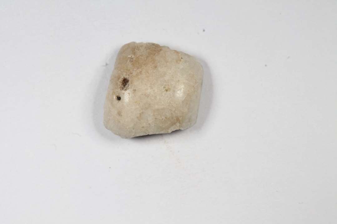 Fragment af cylindrisk, uigenemsigtig, hvid-grå glasperle. Største mål: 1 cm.