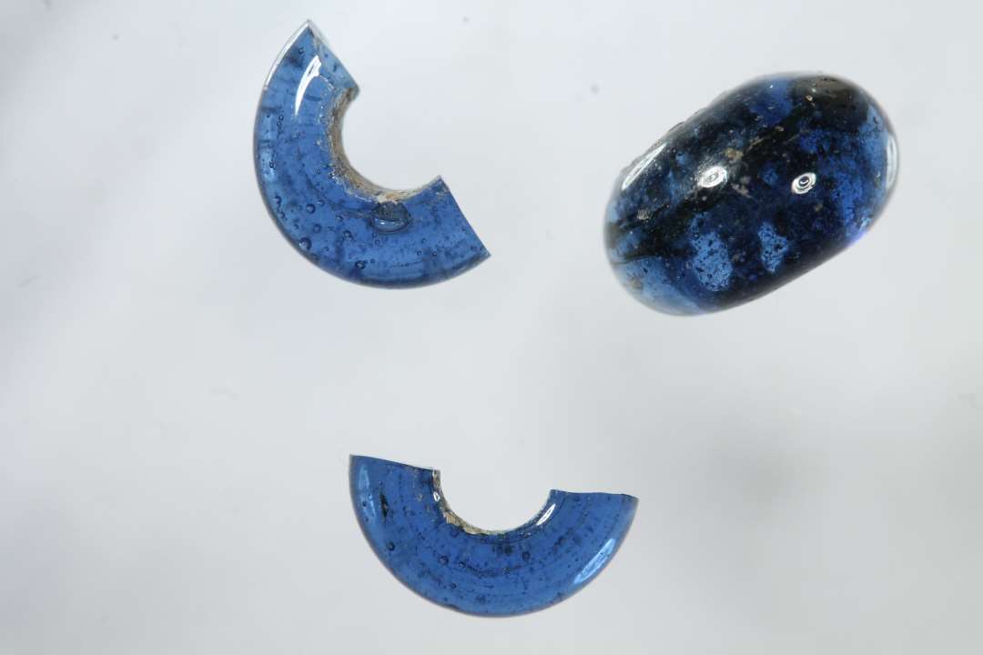 Halv ringformet, gennemsigtig, blå glasperle. Diameter: ca 1 cm.