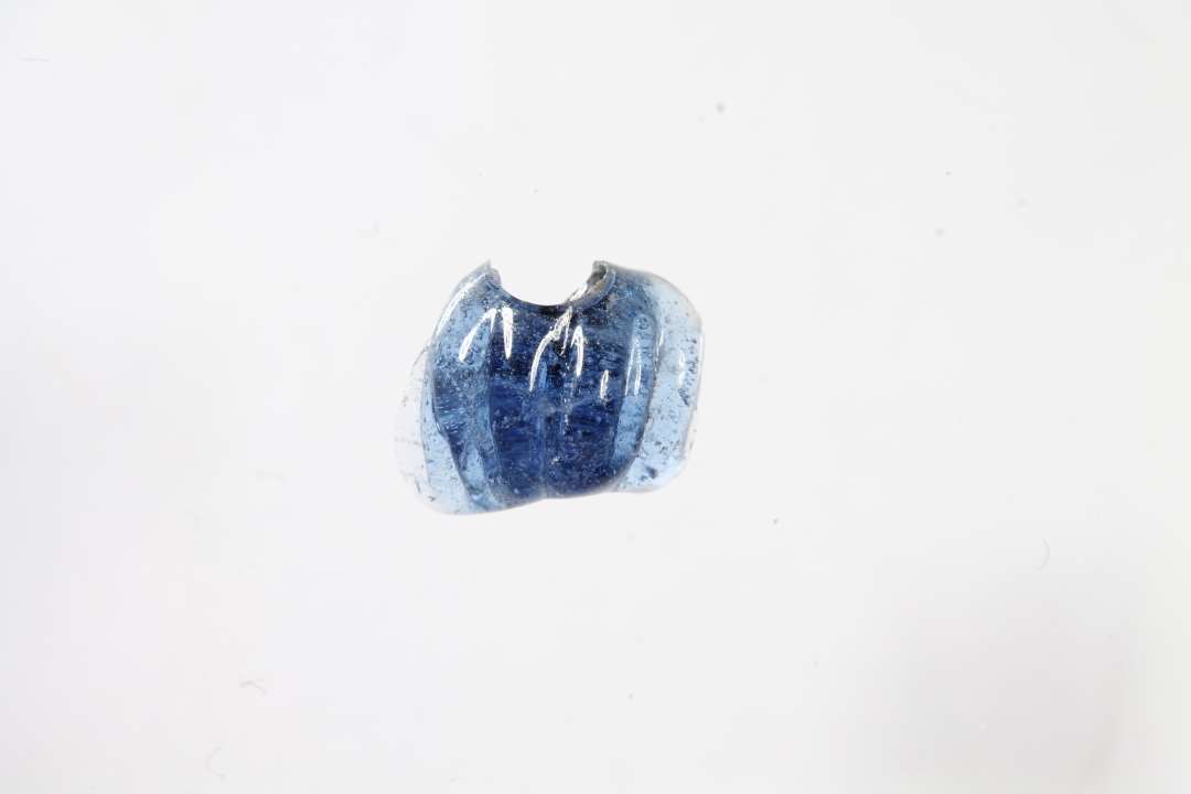 Fragment af ringformet, melonformet, gennemsigtig blå glasperle. Største mål: 0,7 cm.