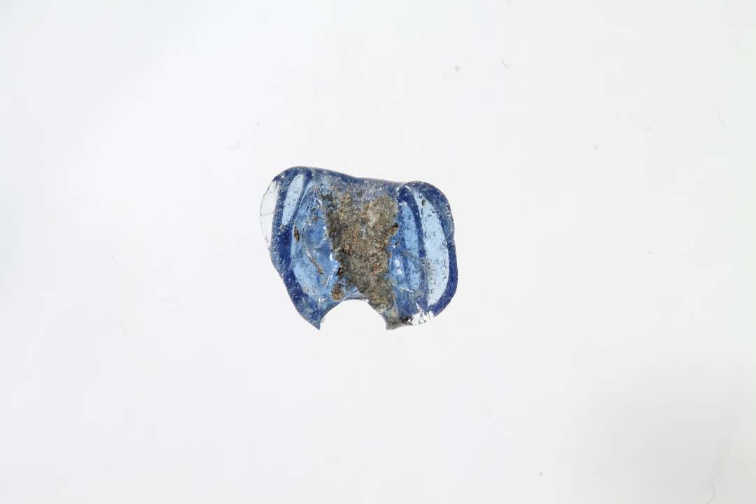 Fragment af ringformet, melonformet, gennemsigtig blå glasperle. Største mål: 0,7 cm.