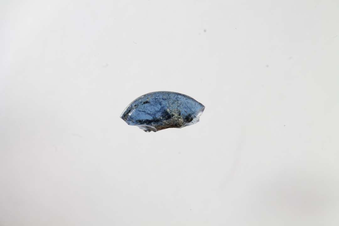 Fragment af ringformet gennemsigtig blå glasperle. Største mål: 0,7 cm.