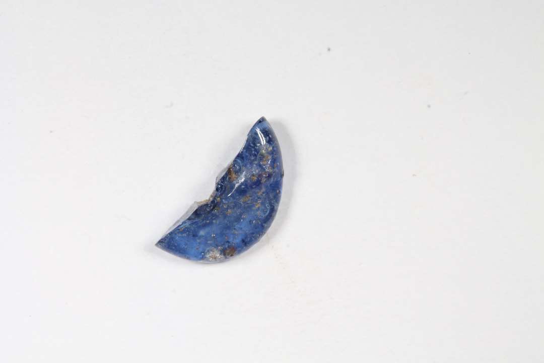 Halv ring- eller skiveformet, gennemsigtig blå glasperle. Diameter: 1 cm.
