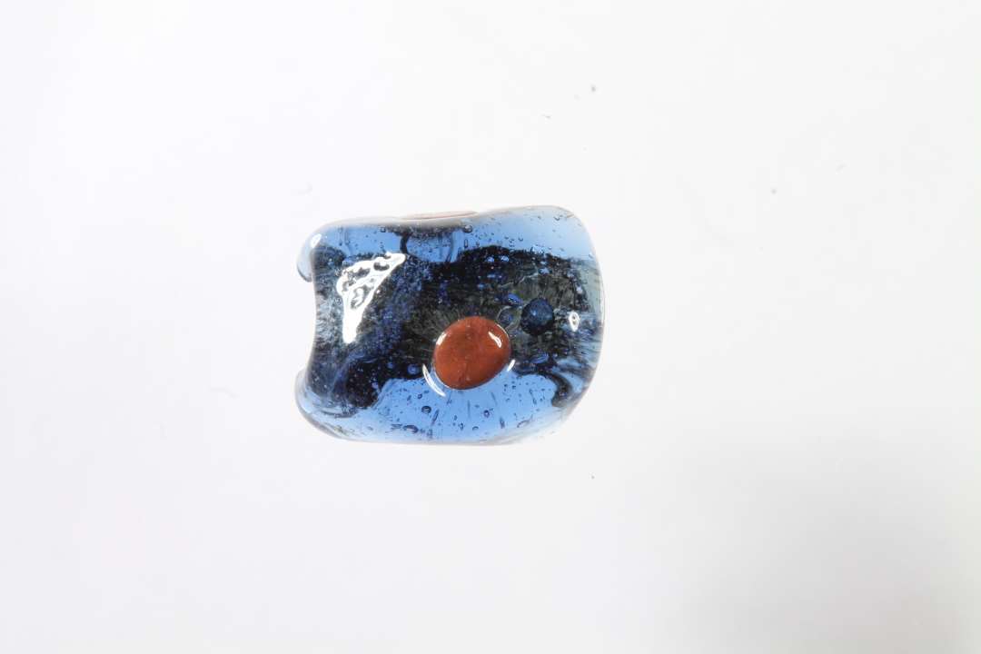 Halv polyhydrid, polyedrisk, gennemsigtig blå glasperle med rødt. Største mål: 1,1 cm.