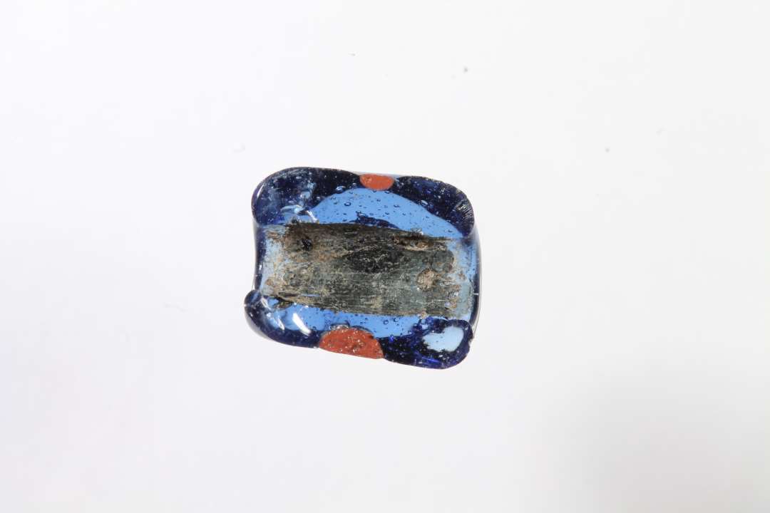 Halv polyhydrid, polyedrisk, gennemsigtig blå glasperle med rødt. Største mål: 1,1 cm.