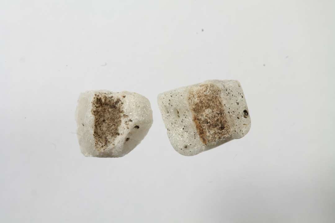 To fragmenter af cylindriske, uigennemsigtige hvidgrå glasperler