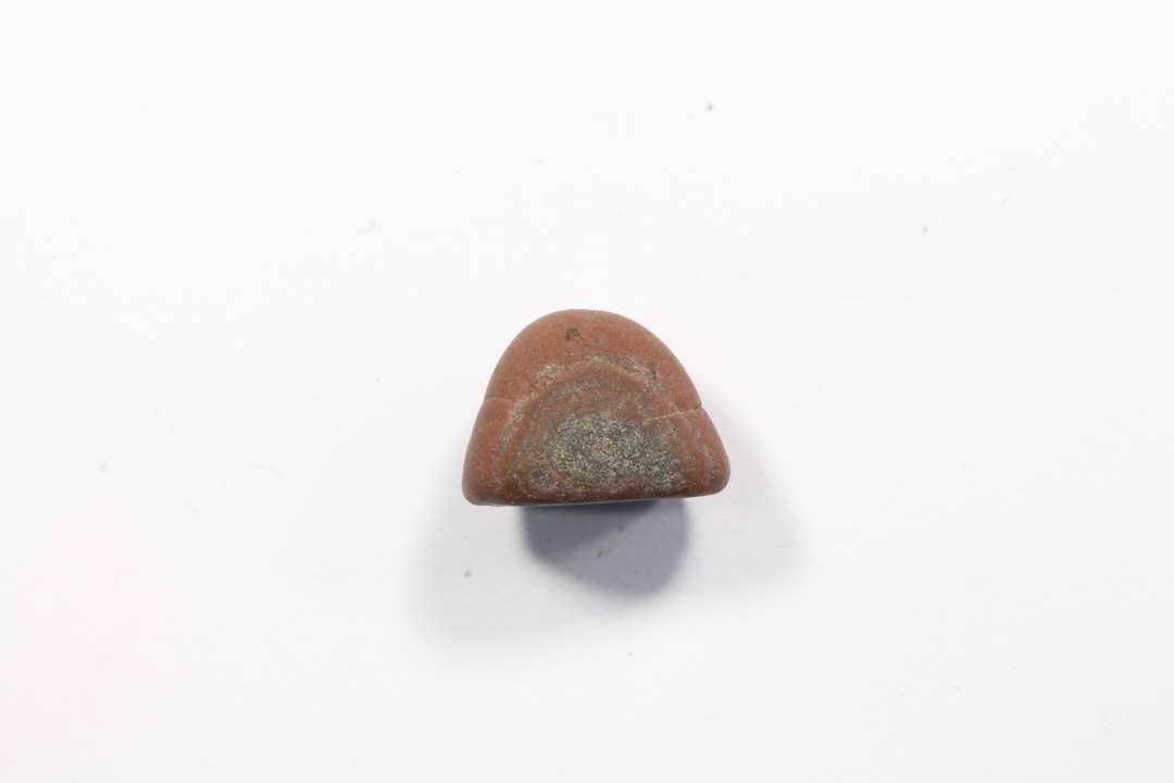 Granitstykke af rød granit. Glat, rund, blød. Tildannet? spillebrik? Største mål: 1,3 cm.