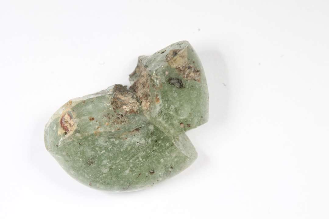 Fragment af ringformet, meget stor og uregelmæssig, halvgennemsigtig, lysegrøn glasperle. Sammenlimet af to stykker. Diameter: 1,6 cm.