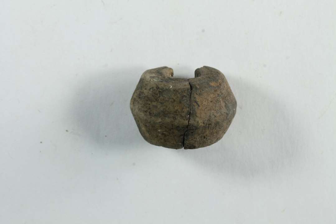 Fragmenteret tenvægt af ler. Dobbeltkonisk. 3/4 del bevaret. To sammenlimede stykker. diameter: 2,6 cm.