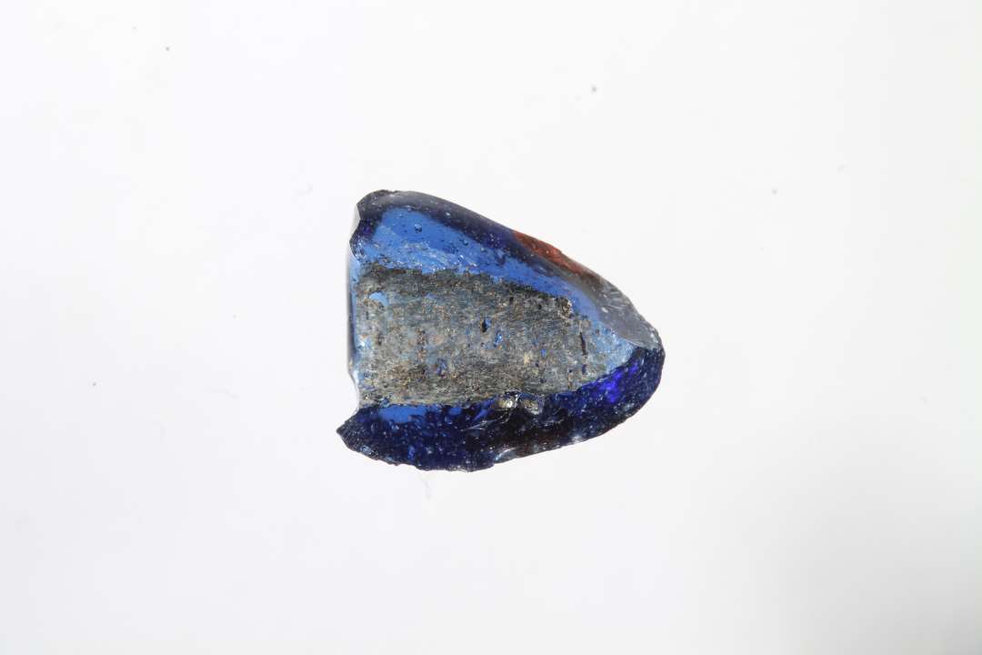 Fragment af polyhydrid, polyedrisk, gennemsigtig blå glasperle med rød prik