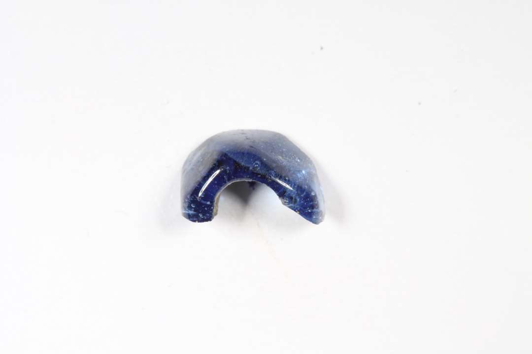 Fragment af polyhydrid, polyedrisk, gennemsigtig, blå glasperle. Største mål: 0,9 cm.
