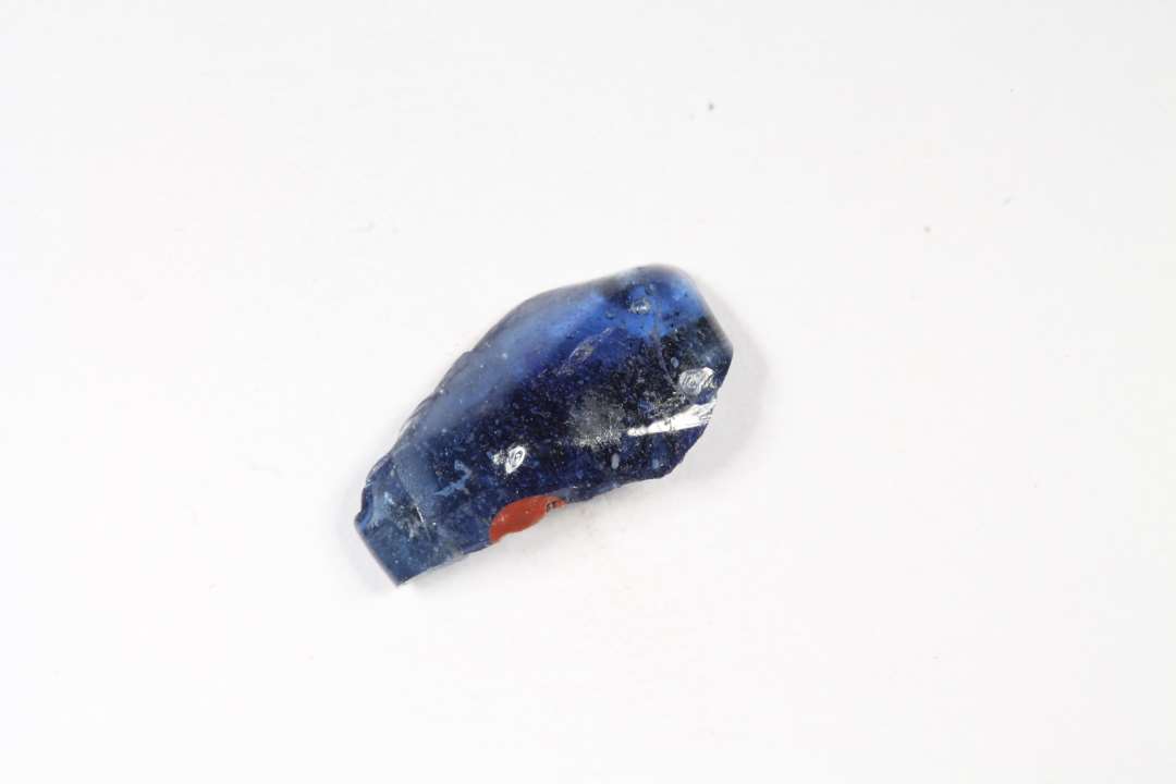 Fragment af polyhydrid, polyedrisk, gennemsigtig glasperle. blå med rødt. Største mål: 1,3 cm.