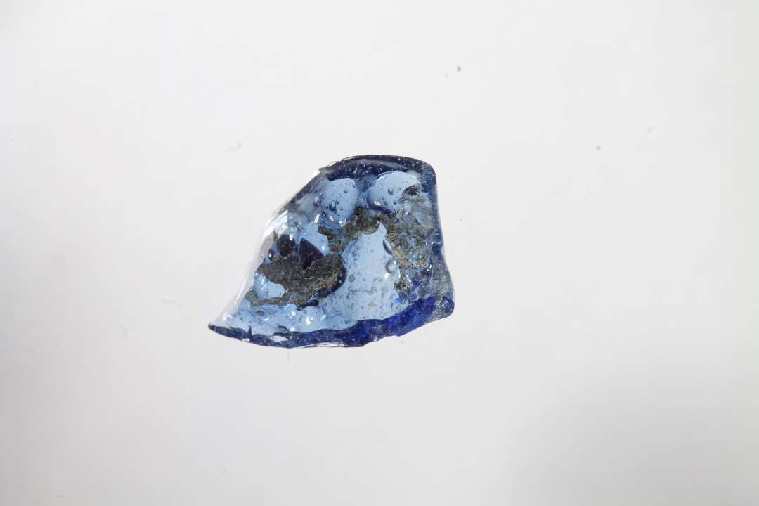 Fragment af ployhydrid, polyedrisk, gennemsigtig blå glasperle med rød prik