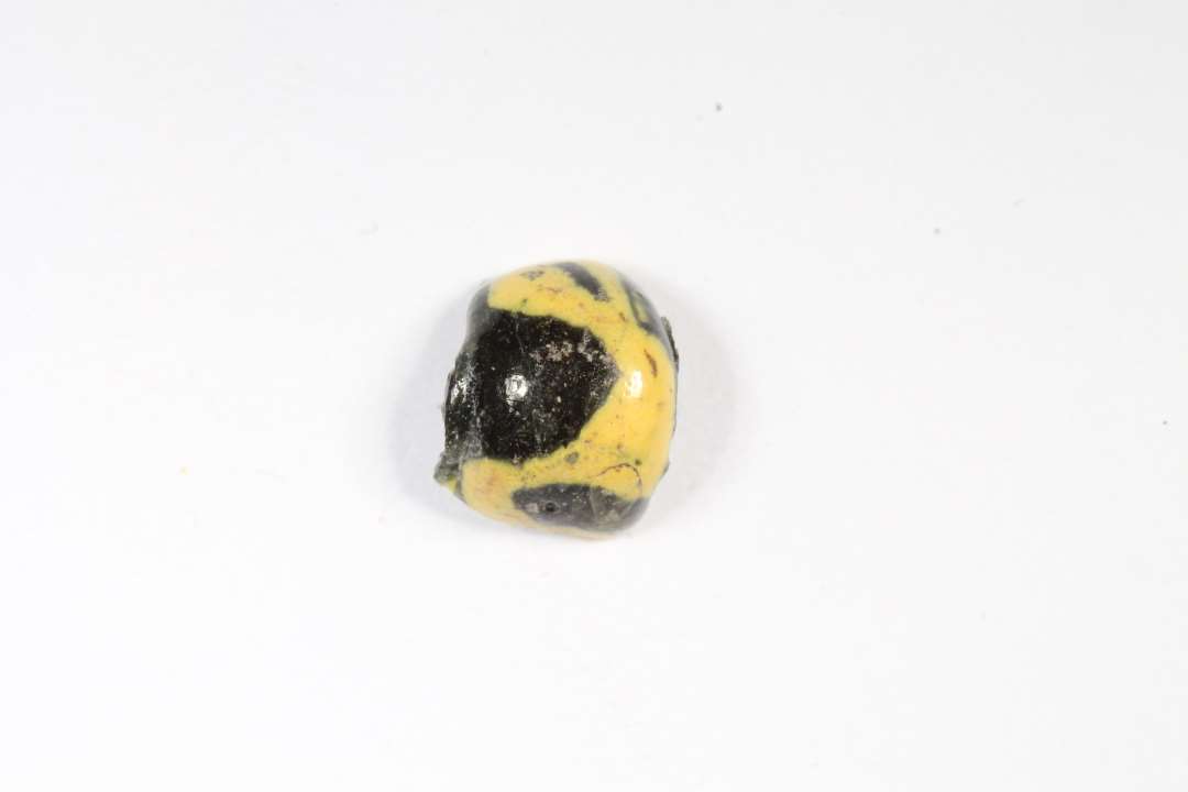 Halv cylindrisk, uigennemsigtig sort glasperle med gult. Største mål: 0,8 cm.