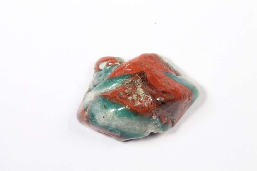 To fragmenter af samme dobbeltkoniske, uigennemsigtige glasperle, rød, mixet glasmasse med grønt og hvidt. Diameter: 1,3 cm. Sammenlimede