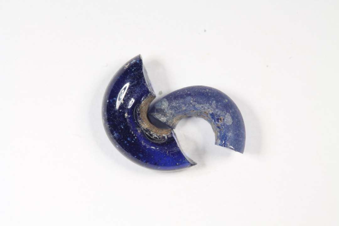To halve ringformede, gennemsigtige eller halvgennemsigtige blå glasperle. Diameter: 0,9 og 1,2 cm. Den ene slidt/nedbrudt i overfladen