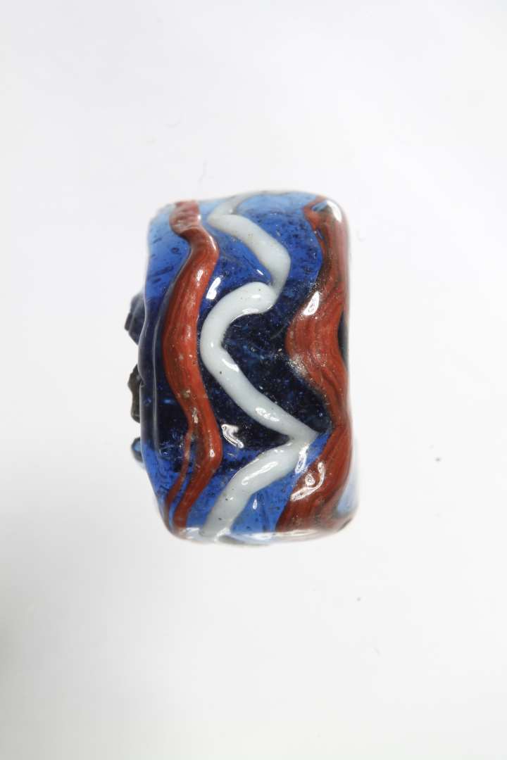 Halv cylindrisk ribeperle. Gennemsigtig blå med rød og hvid dekoration. Diameter: 1,4 cm.