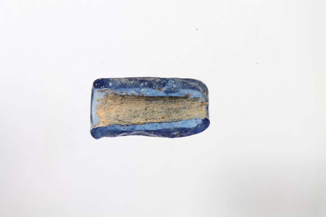 Halv cylindrisk, gennemsigtig blå glasperle. Længde: 1,1 cm.