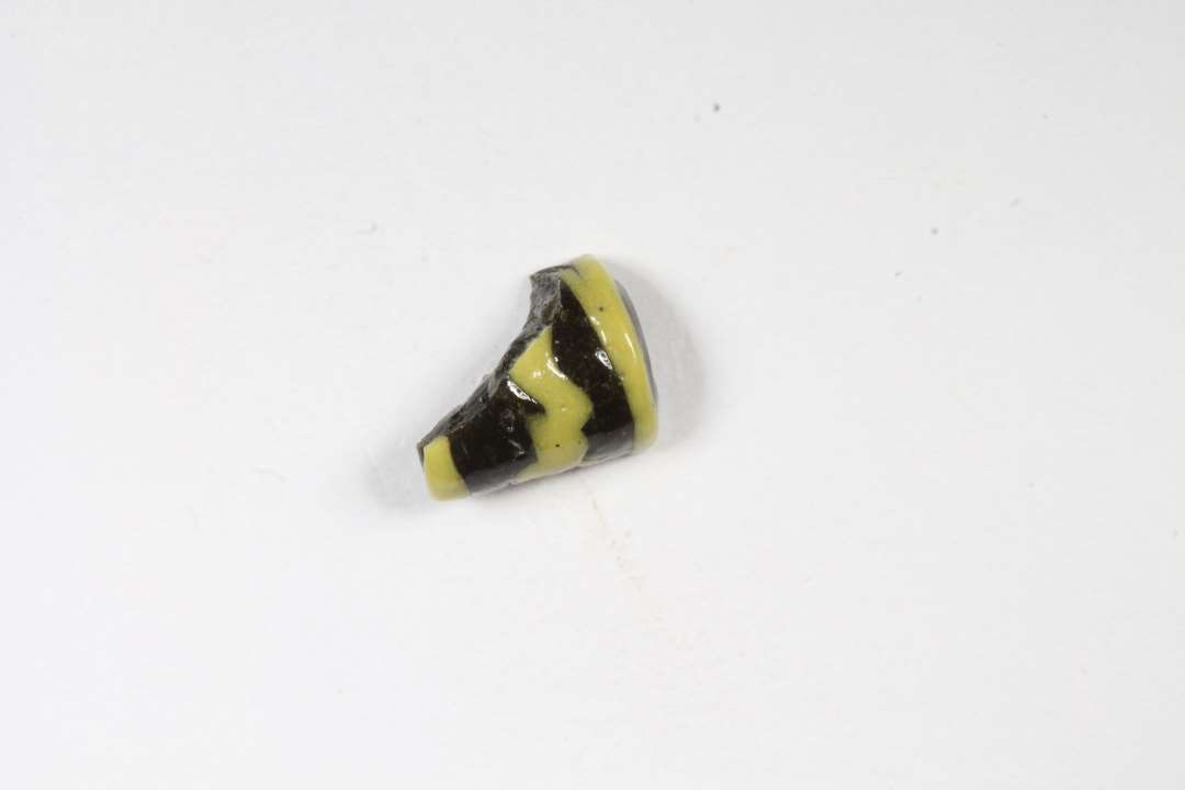 Fragment af cylindrisk hvepseperle. Uigennemsigtig. Sort med gult. Største mål: 0,6 cm.