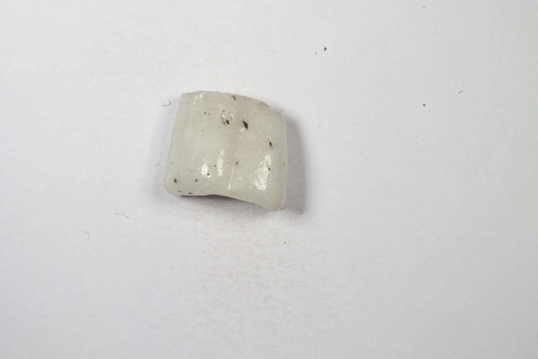Fragment af cylindrisk melonformet, uigennemsigtig hvidgrå glasperle. Diameter: 0,8 cm.