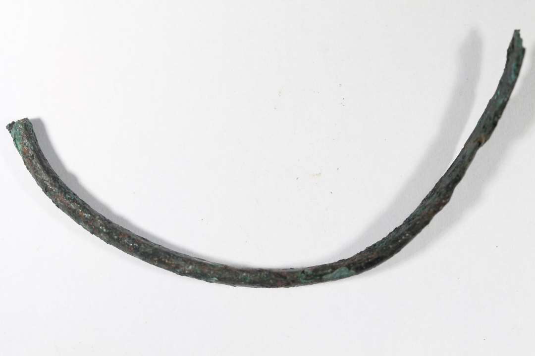 Fragment af simpelt, båndformet armring af bronze. halvdelen bevaret. Cirkulært til fladt tværsnit. Igen ornamentik. Diameter: 6,5 cm., bredde: 0,7 cm.