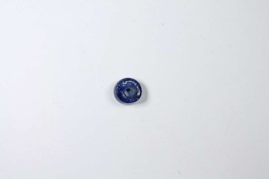 Afskåret gennemsigtig blå glasperle. Diameter: 0,4 cm.
