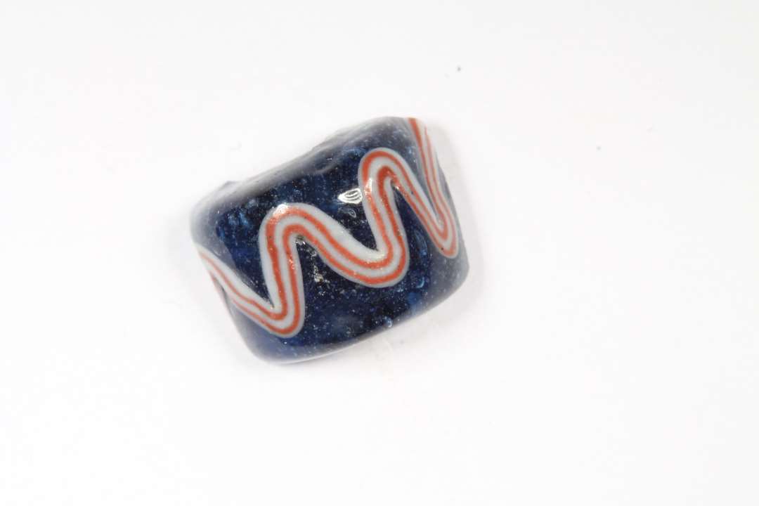 Fragment af cylindrisk ribeperle. Gennemsigtig, blå med hvidt og rødt. diameter: 1,1 cm.