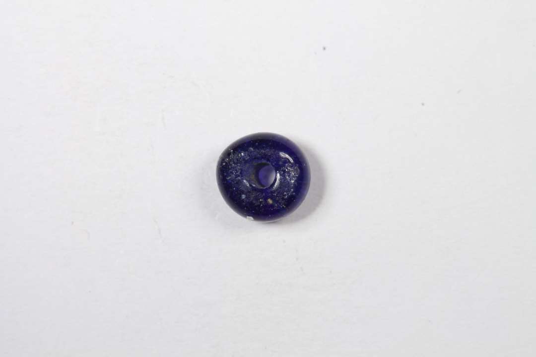 Ringformet, afskåret, halvgennemsigtig blå glasperle. Diameter: 0,5 cm.