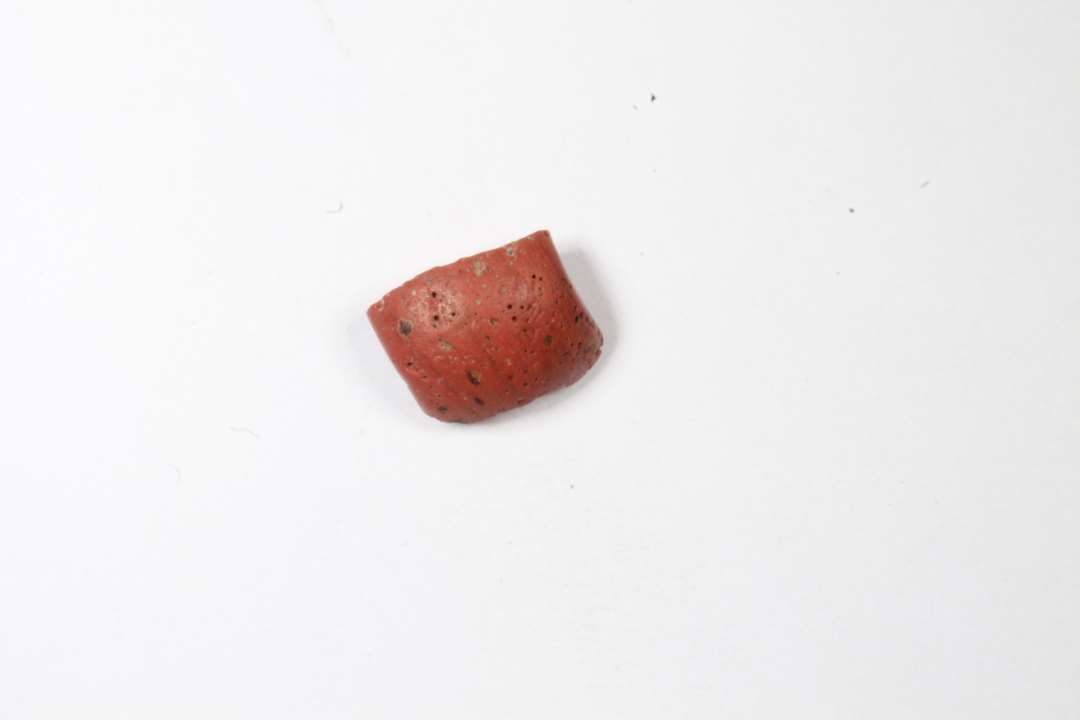 Fragment af tøndeformet, uigennemsigtig rødbrun perle. Mål: 0,7 cm.