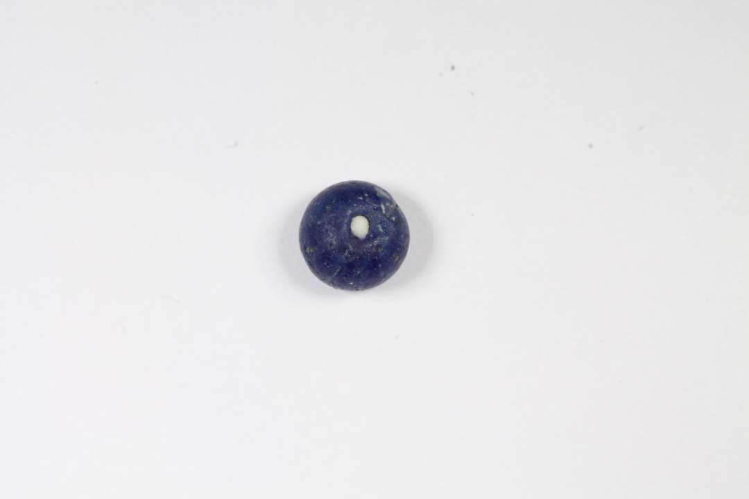 Afskåret, ringformet, halvgennemsigtig, blå glasperle. Diameter: 0,5 cm.