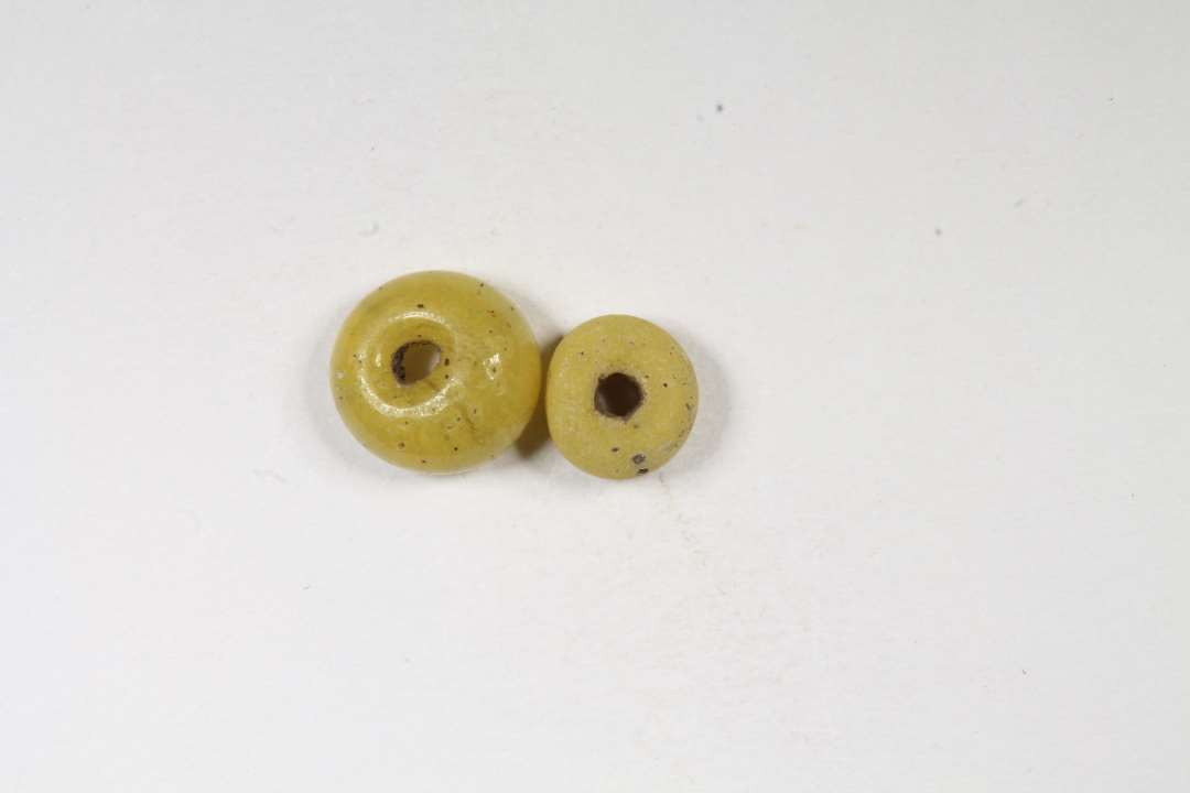 Afskåret, ringformet, uigennemsigtig, gul glasperle. Diameter: 0,5 og 0,6 cm.