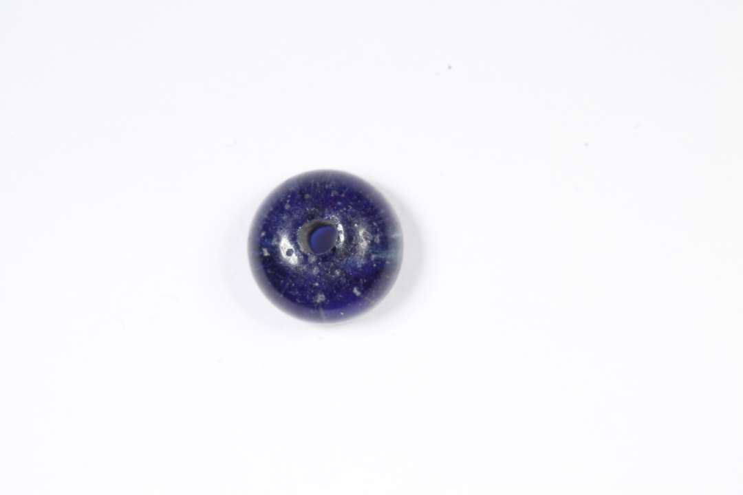 Ringformet, afskåret, halvgennemsigtig, blå glasperle. Diameter: 0,6 cm. 