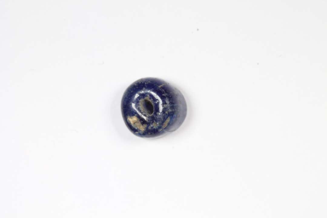 Cylindrisk, afskåret, halvgennemsigtig, blå glasperle. Diameter: 0,6 cm.
