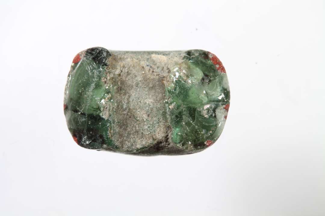 Halv tøndeformet, halvgennemsigtig grøn glasperle med rødt og hvidt. Diameter: 1,6 cm.