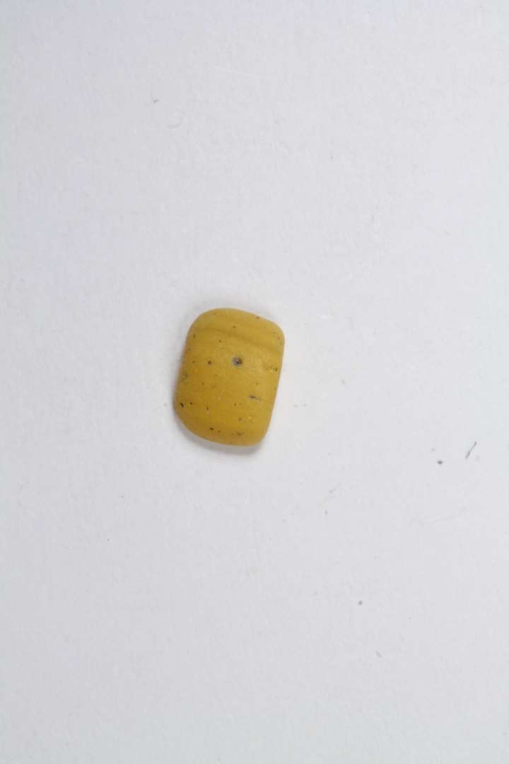Fragment af lille cylindrisk uigennemsigtig gul glasperle. Største mål: 0,5 cm.