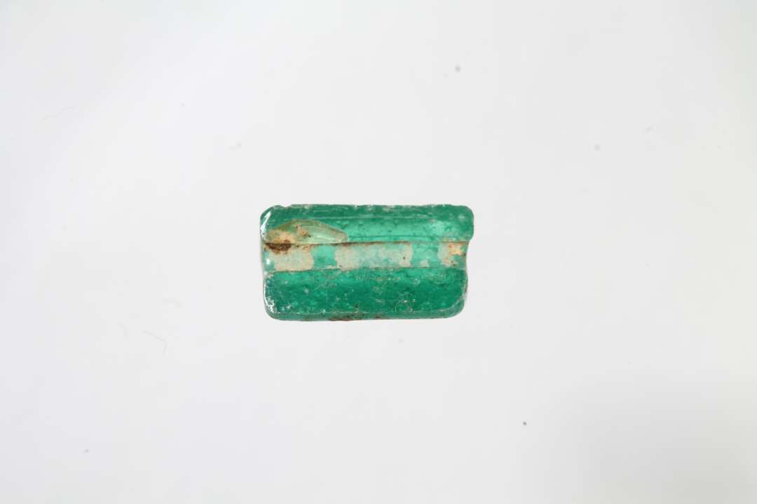 Halv cylindrisk, halvgennemsigtig grøn glasperle. Længde: 0,8 cm.