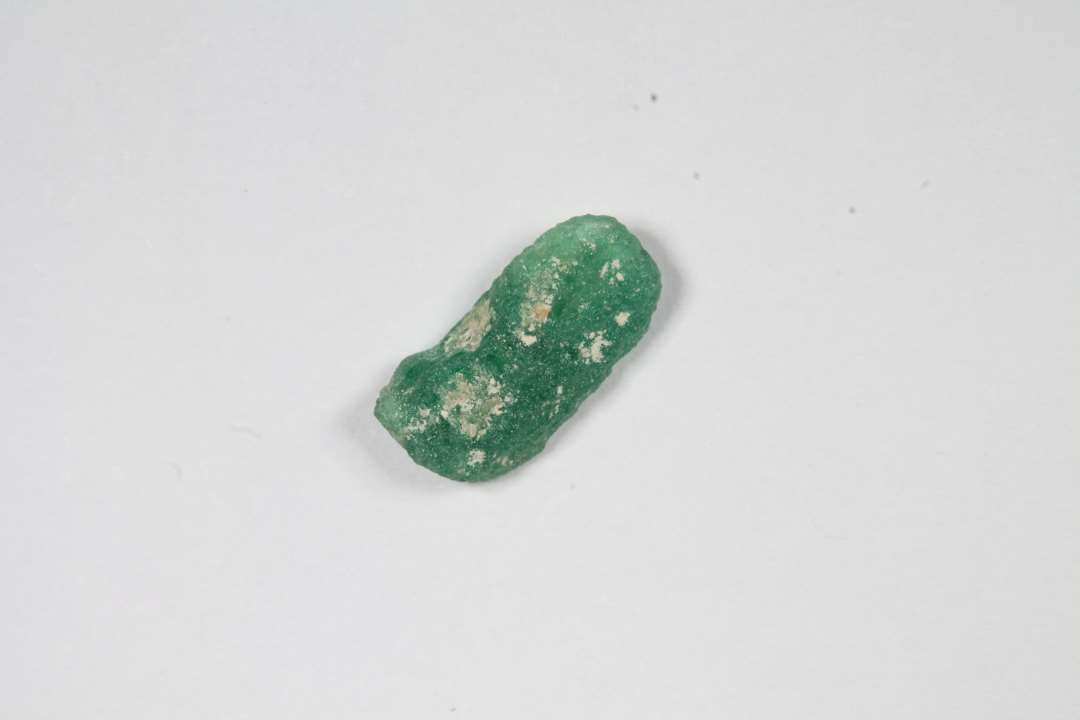 Fragment af cylindrisk eller cylindrisk kubisk, halvgennemsiigtig grøn glasperle. Halvt smeltet/deform