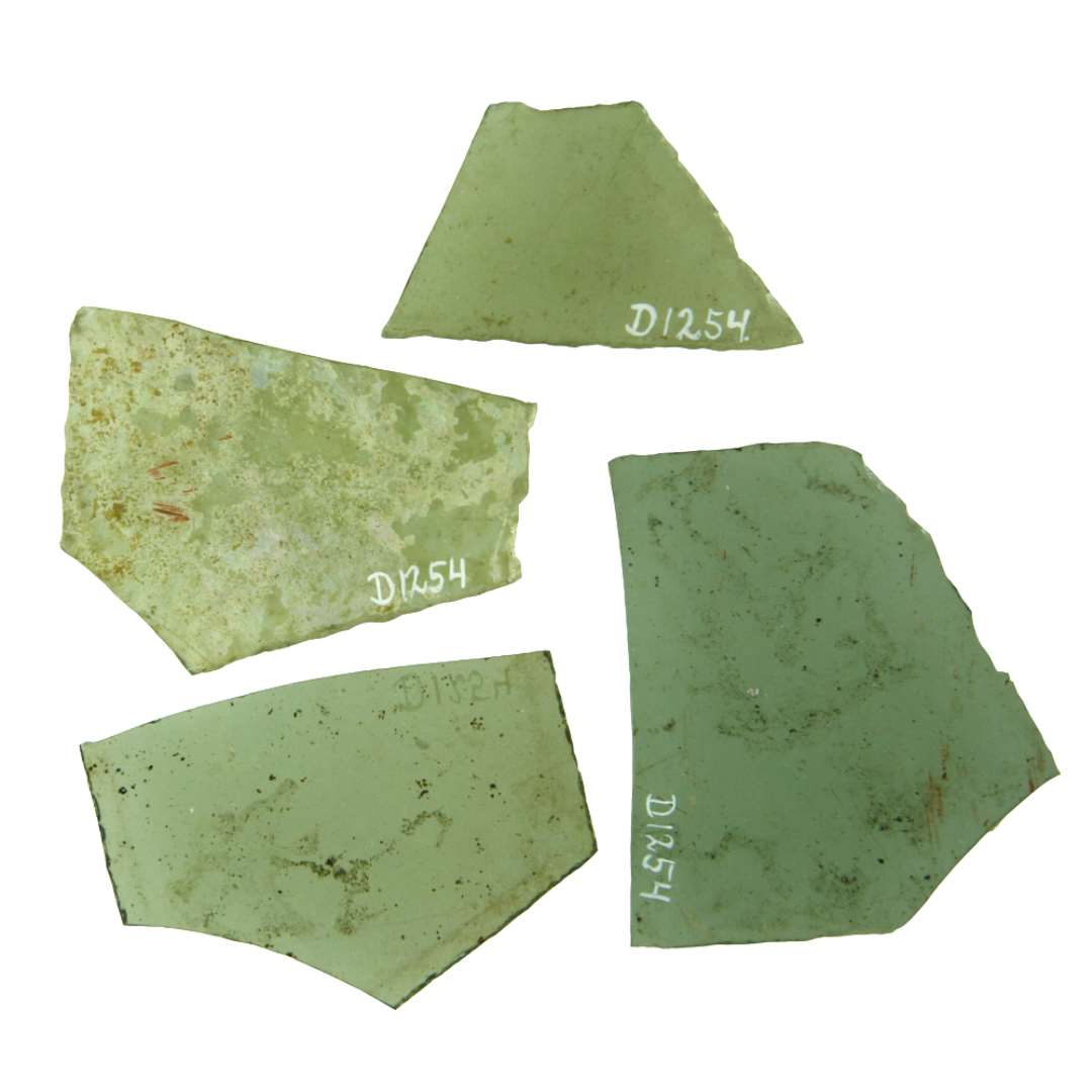 4 fragmenter af ruder af klart, grønligt glas med afnsppede kanter, antagelig alle af trapetzform. De tre af rudefragmenterne har det spidse hjørne afbrudt.