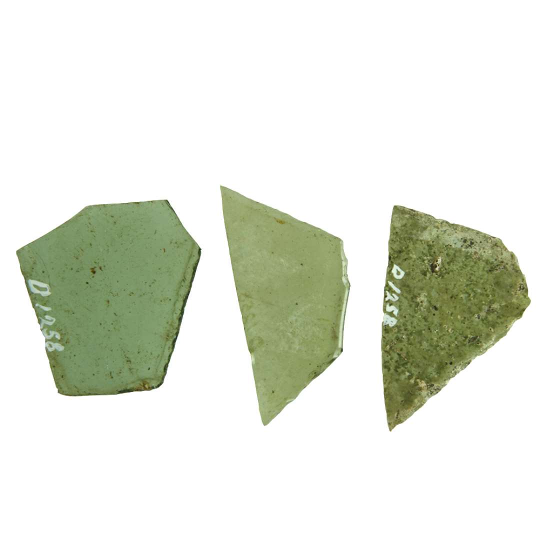 24 rudefragmenter af klart, grønligt  glas med afnappede kanter. Fragmenterne udviser kun en bevaret side, der mødes med de delvise afbrudte sider i 2 stumpe vinkler. Fragmenterne hidrører antagelig fra ruder af 5 eller 6 sidet form.