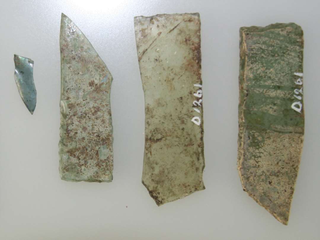 13 rudefragmenter af klart grønligt glas med afnappede kanter. 6 af fragmenterne udviser 2 retvinklede hjørner, 5 fragmenter udviser 1 retvinklet hjørne, 2 fragmenter udviser 2 retvinklede  og 1 stumpvinklet hjørne.